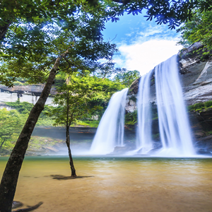 Beeindruckender Wasserfall inmitten üppiger Natur Ein majestätischer Wasserfall fließt in einen klaren Teich, umgeben von dichter grüner Vegetation und strahlendem blauen Himmel.